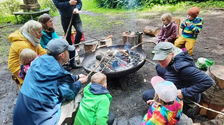 Eine Gruppe Erwachsener und Kinder grillen Würstchen am Sttock über einem offenen Feuer in einer Metallschale | © Sebastian Grumbrecht